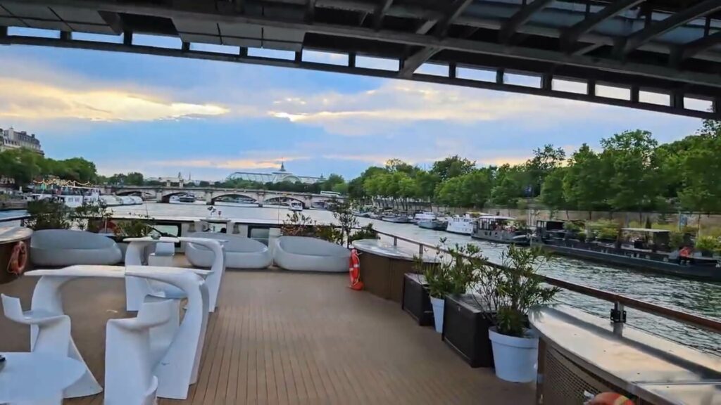 Vue du rooftop aménagé avec banquettes, tables et vue panoramique sur Paris illuminé